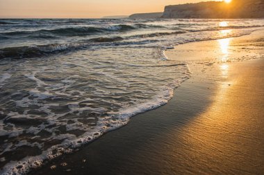 Gün batımı sırasında kumsala yaklaşırken dalgalar