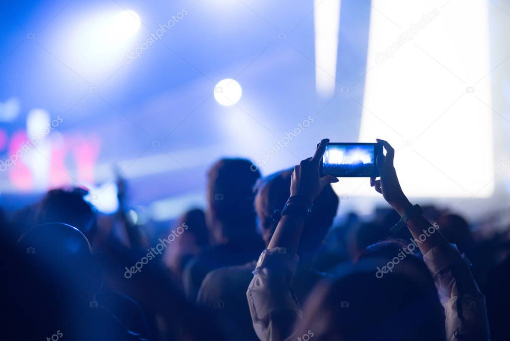 Silhouette of raised hands holding a smart phone recording music