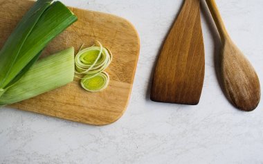Sağlıklı yemekler pişirmek. Dilimlenmiş ve doğranmış pırasa beyaz arka plan izole ahşap kesme tahtası üzerinde yeşil salata ile
