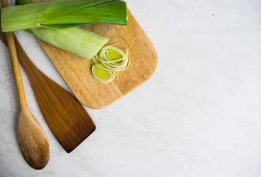 Sağlıklı yemekler pişirmek. Dilimlenmiş ve doğranmış pırasa beyaz arka plan izole ahşap kesme tahtası üzerinde yeşil salata ile