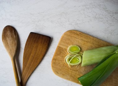 Sağlıklı yemekler pişirmek. Dilimlenmiş ve doğranmış pırasa beyaz arka plan izole ahşap kesme tahtası üzerinde yeşil salata ile