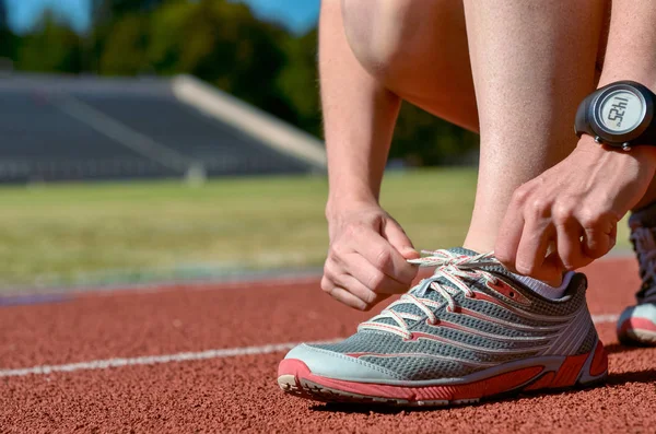 Zapatillas de running primer plano, atleta corredora femenina atando cordones para entrenar y trotar en pista de estadio, deporte y fitness concepto —  Fotos de Stock