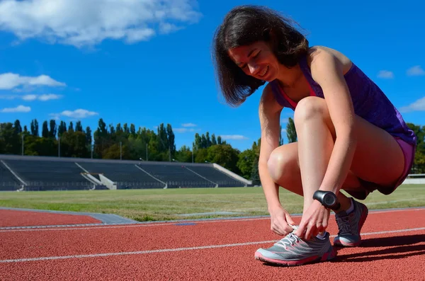 Deportista corredora atando cordones de zapatillas de running para entrenar y trotar en pista de estadio, deporte y fitness — Foto de Stock
