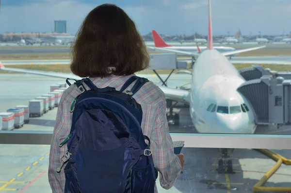 Kobieta w terminalu lotniska czekając na lot i patrząc na samolot, turysta koncepcja — Zdjęcie stockowe