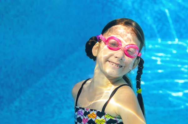 Criança nada na piscina sob a água, engraçado menina feliz em óculos se diverte e faz bolhas, esporte infantil em férias em família ativa — Fotografia de Stock