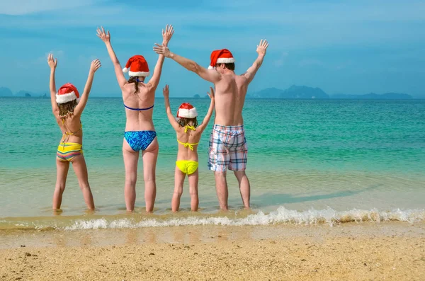 Family vacation on Christmas and New Year holidays, happy parents and children in santa hats have fun on beach, travel with kids — Stock Photo, Image