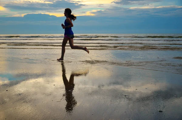 Silhouette di donna che corre jogger sulla spiaggia al tramonto con riflessione, fitness e concetto di sport — Foto Stock