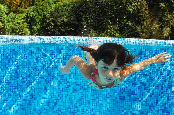 Child swims in pool underwater, happy active girl dives and has fun in water, kid fitness and sport on family vacation