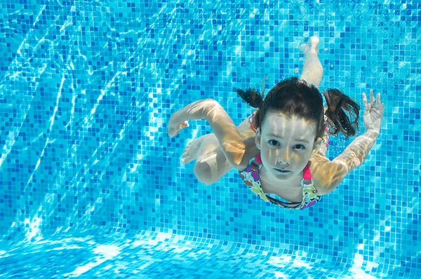 Niño nada en la piscina bajo el agua, inmersiones de chica activa feliz y se divierte, fitness para niños y deporte en vacaciones en familia —  Fotos de Stock