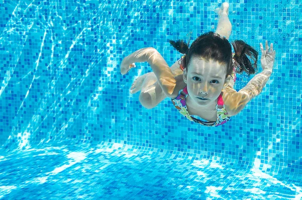 Niño nada en la piscina bajo el agua, inmersiones de chica activa feliz y se divierte en el agua, fitness para niños y deporte en vacaciones familiares — Foto de Stock