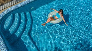 Yukarıdan, yüzme havuzunda güzel kızın havadan görünümü şişme halka çörek üzerinde yüzmek ve su eğlenceli ailecek tatile vardır