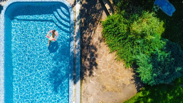 Vista aerea della ragazza in piscina dall'alto, bambino nuotare sulla ciambella anello gonfiabile e si diverte in acqua in vacanza in famiglia — Foto Stock