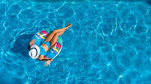 Aerial top view of beautiful girl in swimming pool from above, relax swim on inflatable ring donut and has fun in water on family vacation