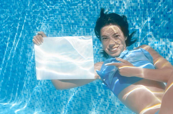 Belle jeune fille tenant tableau blanc dans la piscine sous l'eau, fitness et plaisir en vacances en famille — Photo