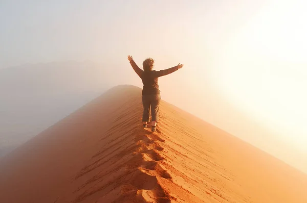 Personen står ovanpå dune i öknen och tittar på stigande solen i dimma med händer upp, resor i Afrika, Namibia — Stockfoto