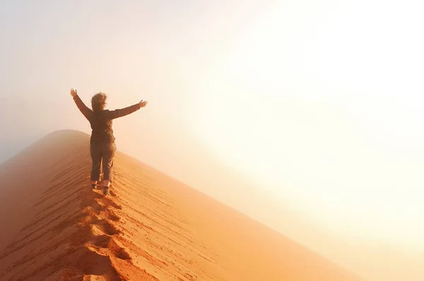 Person, die auf einer Düne in der Wüste steht und mit erhobenen Händen die aufgehende Sonne im Nebel betrachtet, reist in Afrika, Namibia — Stockfoto