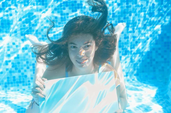 Güzel genç kız yüzme havuzunda beyaz boş bir tahta tutuyor. Su altında, spor salonunda ve aile tatilinde.