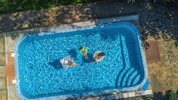 Aerial top view of family in swimming pool from above, happy mother and kids swim on inflatable ring donuts and have fun in water on family vacation