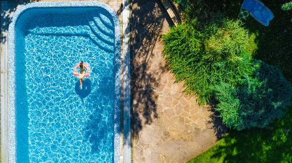Aerial top view of little girl in swimming pool from above, kid swims on inflatable ring donut , child has fun in water on family vacation resort