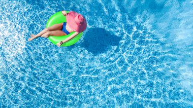 Yüzme havuzunda şapkalı güzel bir kadın yukarıdan havuz manzaralı, bikinili genç bir kız şişme yüzüklü çörek yiyor ve aile tatilinde suda eğleniyor, tropikal tatil beldesinde.