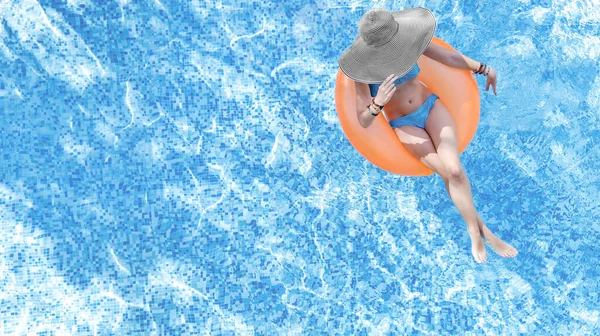 Beautiful woman in hat in swimming pool aerial top view from above, young girl in bikini relaxes and swims on inflatable ring donut and has fun in water on family vacation, tropical holiday resort