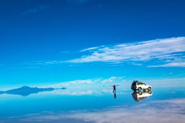Bolivya 'da Salar de Uyuni' de gün doğumu su, araba ve adam tuzlu düz çölde ve gökyüzü yansımalarıyla kaplıdır.