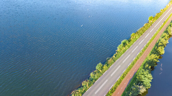 Aerial drone view of motorway road and cycling path on polder dam, cars traffic from above, North Holland, Netherlands