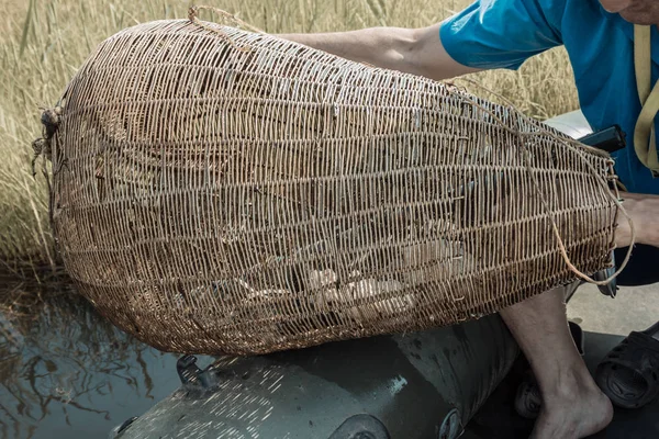 Kıyıda balık tutmak için büyük bir hasır. El işi, dallardan yapılmış eski bir cihaz. Lastik teknedeki bir balıkçı balığı yakalar. Yaz günü, güneşli aydınlatma.