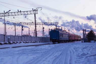 Tren istasyonu, kompozisyon bozulur, trenin son vagonları görünür hale gelir. Kar altında, soğuk bir kış akşamı.