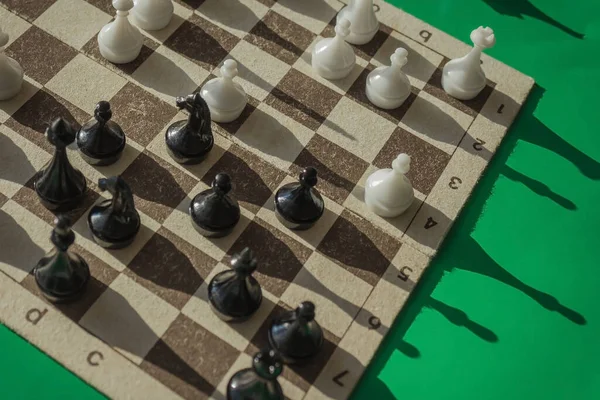 On the chessboard are black and white figures, the game is in full swing. Analysis of the situation, logical thinking. Green background, top view.