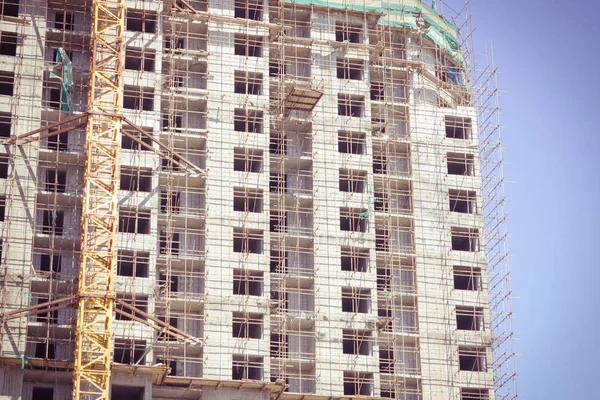 A large concrete house in the scaffolding. Construction industry, real estate, shared construction. Bright sunny day, blue sky, copy space.