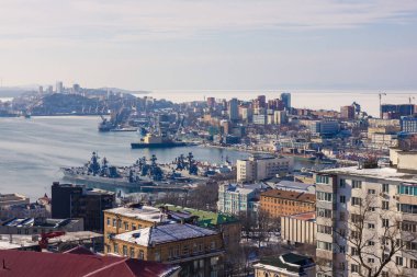 Vladivostok, Pasifik Donanması 'nın üssü, Rusya. Limanda birkaç gemi ayakta duruyor. Kıyıda deniz kenarında birçok modern binalar vardır. Yumuşak güneş ışığı.
