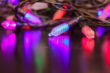 Noel süsleri, farklı renklerde uzun küçük lambalar. Parlak bir arka plan, leylak rengi. Sanatsal resepsiyon bozulması.