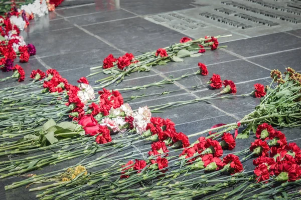 Memorial, eternal memory of the heroes of war, Victory Day. Red, scarlet flowers on gray granite, marble. Daylighting, vignetting.