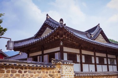 Büyük bir Kore evi, geleneksel mimari. Döşemeleri olan bir çatı. Doğal taş çitler, antik duvarcılık. Mavi gökyüzü, güneşli ışık.