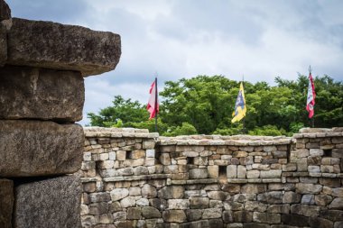 Old fortress wall, rough texture. Top colored flags. Away green trees, sky. Inside view. Vignetting. clipart