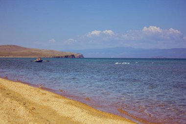 Büyük bir gölün kumlu kıyılarında bir adam ve bir kadınla bir tekne yelken açar. Parlak güneşli bir gün. Yaz. Temiz su. Sahilde büyük sarı kum. Arka planda tepeler var. Bir martı sürüsü suyun üzerinde oturmaktadır. Mavi gökyüzü, küçük 