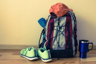 Spor ayakkabılar, bir sırt çantası ve bir şapka yolculuğun başlangıcını bekliyor. Spor, turist ekipmanları, kıyafetler. Geçmişe dönük tonlama.