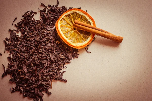 紅茶の黒 乾燥した葉は オレンジとシナモンの棒の円の横にあります 香り高いお茶 伝統的な飲み物 光の背景 暖かいトーン ヴィネット コピースペース — ストック写真