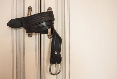 Kaba bir erkek kemeri beyaz kapıların kollarını çeker. Cezalandırılma korkusu, fiziksel etki, yurtiçi terör. Gün ışığı.