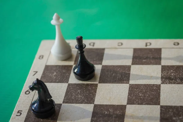 The chess game is over by the rout of the whites. The enemy is cornered, there is no way out. Green background, side lighting.