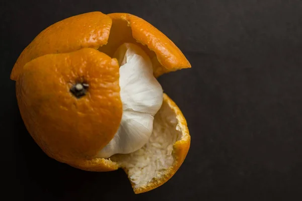 Garlic in a tangerine skin against a dark background. Vain hopes, deception, hypocritical people. View from above.