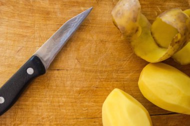 Çizik ve cips dolu eski, tahta bir tahta. Sebze ve çiğ patates temizlemek için keskin bir bıçak. Ev yemeklerini hazırlıyorum. Açık doğal renkler.