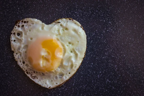 Fried egg in the form of a heart. A good start to the day. Breakfast cooked with love. Dark background, top view.