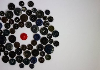 Siyah düğmeler çemberinde, biri kırmızıdır. Bir yabancı, bir casus, bir düşman. Herkes gibi değil. Kuralların çiğnenmesi, kıyafet yönetmeliği, öne çıkma arzusu. Çevreyle yüzleşmek. Üst görünüm, beyaz arkaplan.