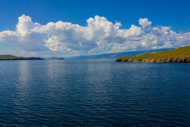 Suyun mavi yüzeyi, yeşil kıyının uzak kısmı. Güneşli bir yaz günü. Burada kimse yok. Gökyüzü açık. Bulutlar.