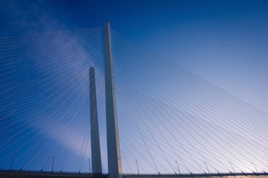 Parlak mavi gökyüzüne karşı modern beton ve çelikten bir köprü. Çelik kablolu iki büyük sütun. Yanal güneş ışığı.