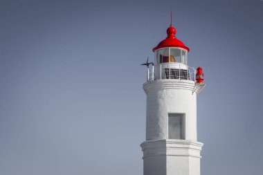 Beyaz tuğlalardan yapılmış eski bir deniz feneri. Tepede kırmızı bir fener var. Doğru yolun işaretidir. Gün, güneş ışığı, alt görünüm, canlanma.