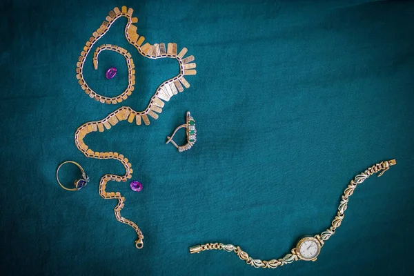 Jewels with emeralds, diamonds, sapphire and gold ladies watches. Dark blue background, vignetting. Products of mass production. View from above.