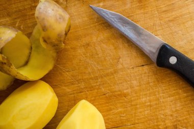 Doğal ahşap, çiğ patates ve sebze temizlemek için bir mutfak bıçağı yüzeyinde. Yemek yapmak, mutfakta çalışmak. Gün ışığı, üst görünüm.